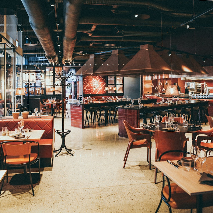 A modern restaurant interior with red leather booths, wooden tables, and hanging pendant lights